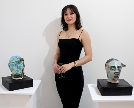 A female student wearing a black dress stands between two sculptures depicting people's faces.